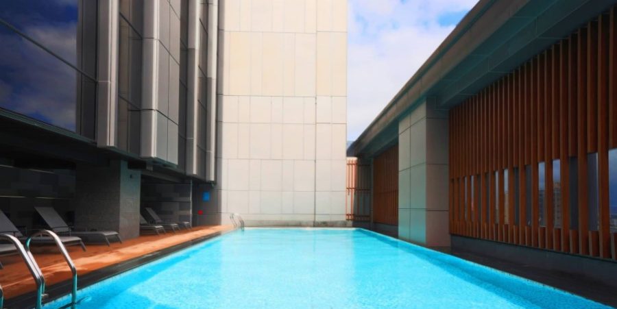 A serene pool located in front of a towering building, reflecting the sunlight on a bright day.